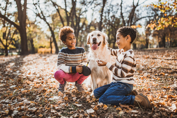 Golden Retriever sitting with two children outside in park